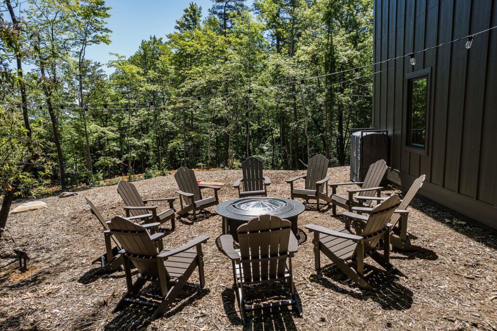 Fire pit in the woods with Adirondack chairs around it.