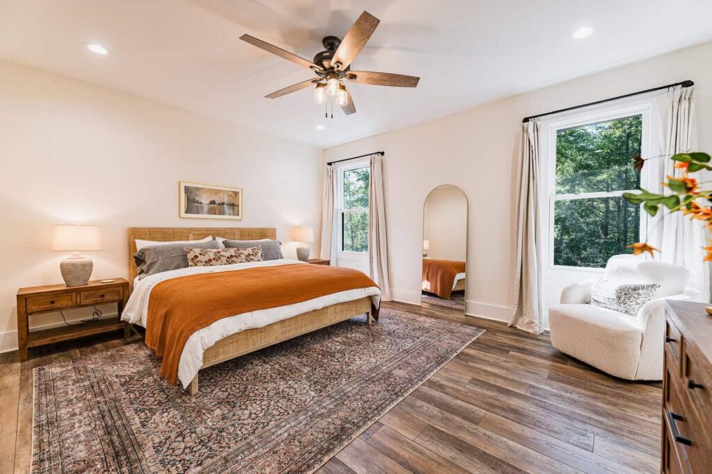 Bedroom with a king bed with white, chambray, and orange bedding, dresser, and swivel chair.
