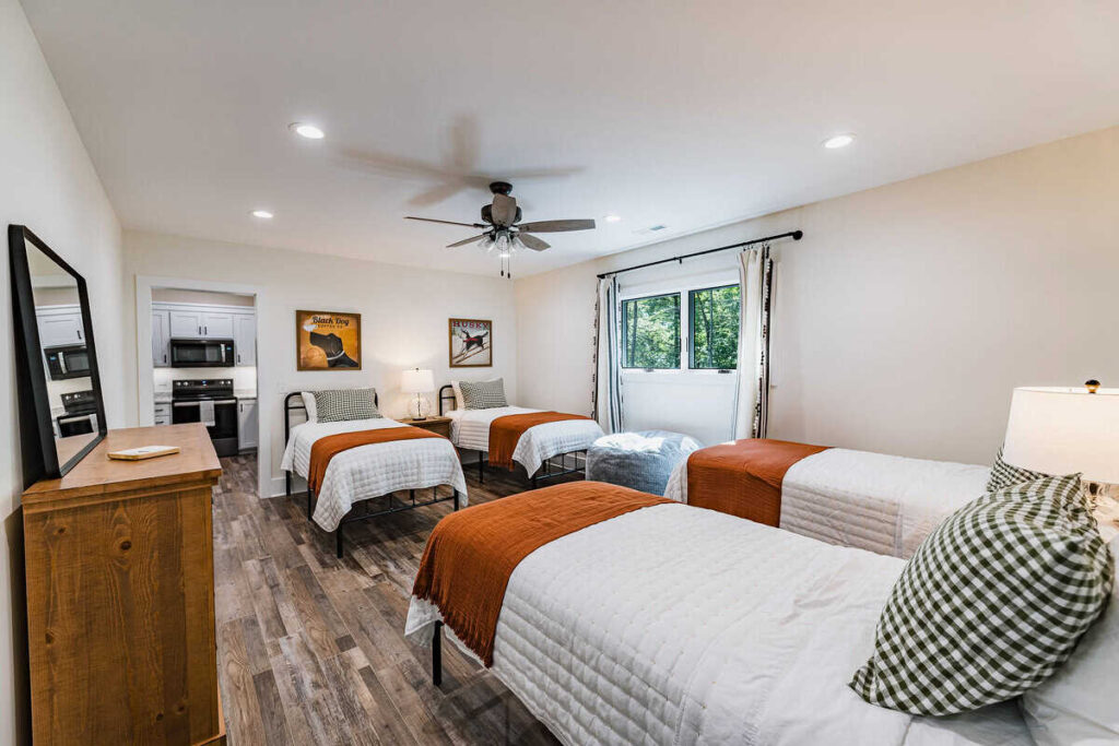 Bedroom with four twin beds topped with green and white gingham pillows and burnt orange coverlets.