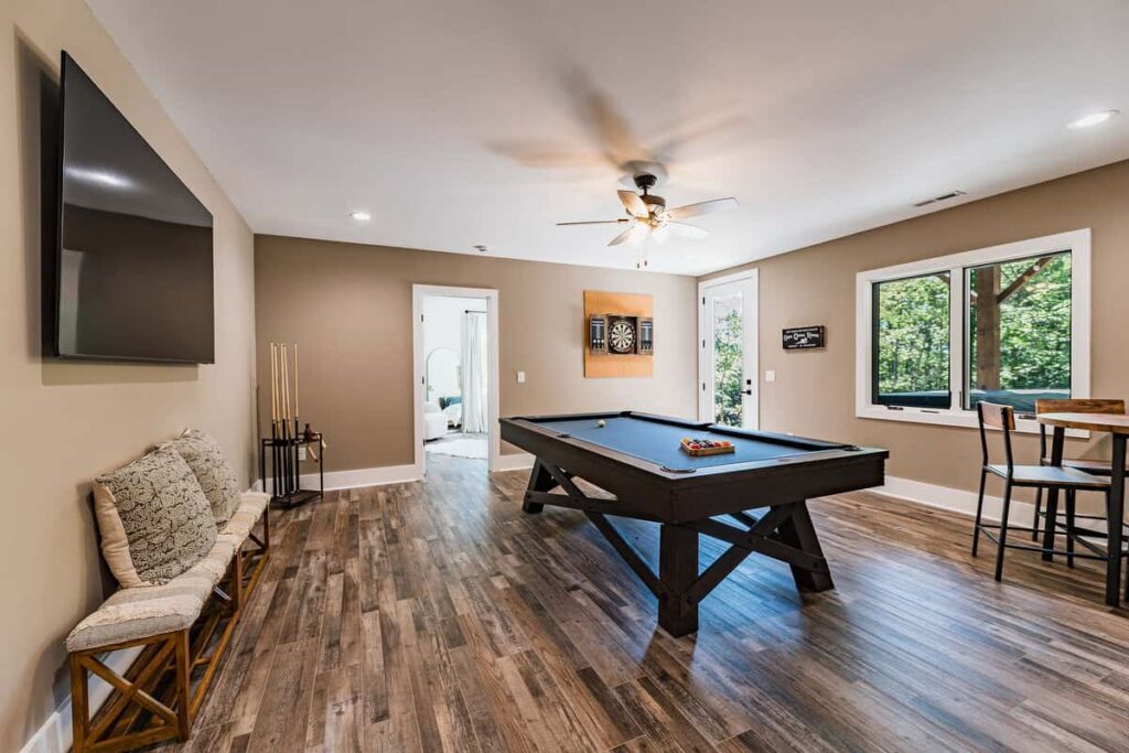Game room with a large TV, table with bar stools, pool table, and dart board.